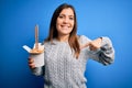 Young woman eating asian noodles from take away box using chopstick over blue background with surprise face pointing finger to