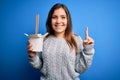 Young woman eating asian noodles from take away box using chopstick over blue background surprised with an idea or question