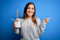 Young woman eating asian noodles from take away box using chopstick over blue background very happy pointing with hand and finger