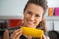 Young woman eating boiled corn in kitchen