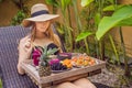 Young woman eating breakfast in a lounge chair on a tray with fruit, buns, avocado sandwiches, smoothie bowl by the pool Royalty Free Stock Photo