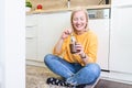 Young woman eating chocolate from a jar while sitting on the wooden kitchen floor. Cute albino girl indulging cheeky face eating