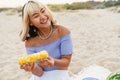 Young woman eating corn during picnic on summer beach Royalty Free Stock Photo