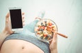 Young woman is eating a fruit salad and using a fitness app on her smartphone after a workout. Royalty Free Stock Photo