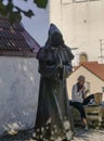 a young woman eating near to a scary monk stuatue on sunny day at old town