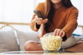 A young woman eating popcorn and searching channel with remote control to watch tv while sitting on sofa at home Royalty Free Stock Photo