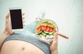 Young woman is eating a salad and using a fitness app on her smartphone after a workout. Royalty Free Stock Photo