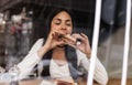 Young woman eating a sandwich in fast food cafe. Cafe window