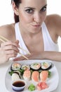 Young woman eating a sushi piece against a white
