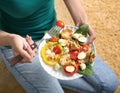 Young woman eating tasty chicken salad with vegetables while sitting on floor Royalty Free Stock Photo