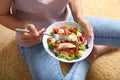 Young woman eating tasty chicken salad with vegetables while sitting on floor Royalty Free Stock Photo