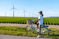 young woman electric green bike bicycle by windmill farm , windmills on a beautiful summer
