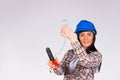 A young woman electrician in a blue hard hat installs a light bulb on a white background with blank space. Gender