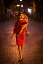 Young woman in elegant red dress holding bouquet of roses while walking on street at night Royalty Free Stock Photo