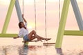 Young woman enjoying sunrise on swing over water Royalty Free Stock Photo