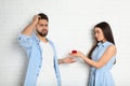 Young woman with engagement ring making marriage proposal to her boyfriend near white wall