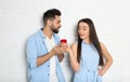 Young woman with engagement ring making marriage proposal to her boyfriend near brick wall