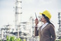 Young woman engineer or construction worker wearing safety hat helmet and holding portable radio with refinery plant background Royalty Free Stock Photo