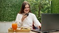 Young woman enjoying breakfast on the terrace while working on her laptop. Concept of freelancing, working remotely, and having a Royalty Free Stock Photo