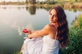 Young woman enjoying glass of wine on river bank at sunset. Woman admiring landscape while having drink Royalty Free Stock Photo