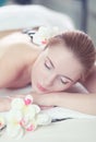 Young woman enjoying a hot rock massage in a spa salon and white flower on her head Royalty Free Stock Photo