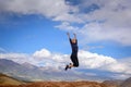 Young woman enjoying life and jumping against blue sky and mountains background. Happy female tourist jumps with hands up on top Royalty Free Stock Photo