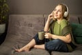 Young woman enjoying listening songs in earphones. Happy millennial teen girl relax with cup of tea and listening music in Royalty Free Stock Photo