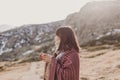 Young woman enjoying nature in mountain covered with a blanket and drinking hot beverage in a mug. relax concept. sunny weather Royalty Free Stock Photo