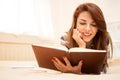 Young woman enjoying reading a book while lying on bed at home. Royalty Free Stock Photo