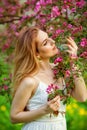 A young woman enjoys life in a spring blooming garden with a background of flowering trees. Young dreamy pensive lady in nature at