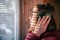 A woman with headphones looks through the blinds at the early morning sunlight. Royalty Free Stock Photo