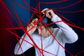 Young woman is entangled in red threads on blue walls background. Concept of obsessive states, paranoia, mental illness Royalty Free Stock Photo