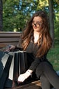 Young woman examines shopping on bench in park. Purchaser. Vertical frame