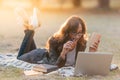 Young woman with eye glasses laying on a the blanket in a park, working with laptop or studying with notebook and books Royalty Free Stock Photo