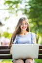 Young woman in eyeglasses sitting on bench in park and using laptop computer Royalty Free Stock Photo