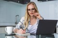 young woman in eyeglasses using laptop and taking notes while working