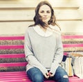 Young woman with face with freckles is siting on a bench. Outdoor picture in full man's length.