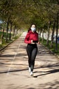 Young woman with face mask because covid, running in the park. Active person outdoors