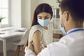 Young woman in face mask getting flu or Covid-19 vaccine at the clinic or hospital