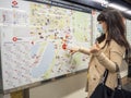 Young woman with face mask pointing in a map inside subway station.