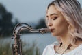 Young woman face profile playing saxophone on bank of the river, female blowing into the trumpet, on nature background, concept