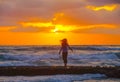 Young woman faces a glorious sunset and heavy surf