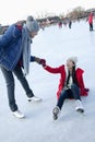 Young woman falls on the ice while skating, boyfriend helps her up