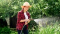 Young woman in farmer hat watering green organic vegetables growing at orchard. People working at backyard garden and Royalty Free Stock Photo
