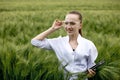 Young woman farmer wearing white bathrobe is checking harvest progress on a tablet at the green wheat field. New crop of wheat is Royalty Free Stock Photo