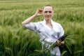 Young woman farmer wearing white bathrobe is checking harvest progress on a tablet at the green wheat field. New crop of Royalty Free Stock Photo