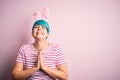 Young woman with fashion blue hair wearing easter rabbit ears over pink background begging and praying with hands together with