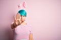 Young woman with fashion blue hair wearing easter rabbit ears over pink background doing stop sing with palm of the hand Royalty Free Stock Photo