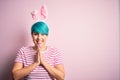 Young woman with fashion blue hair wearing easter rabbit ears over pink background praying with hands together asking for