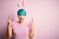 Young woman with fashion blue hair wearing easter rabbit ears over pink background shouting with crazy expression doing rock Royalty Free Stock Photo